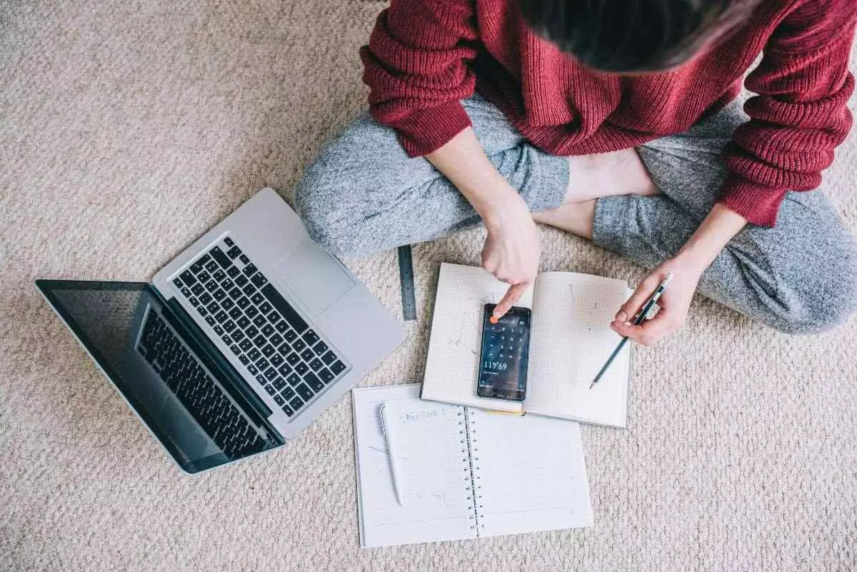 Individual sitting on floor in from of laptop calculating budget.