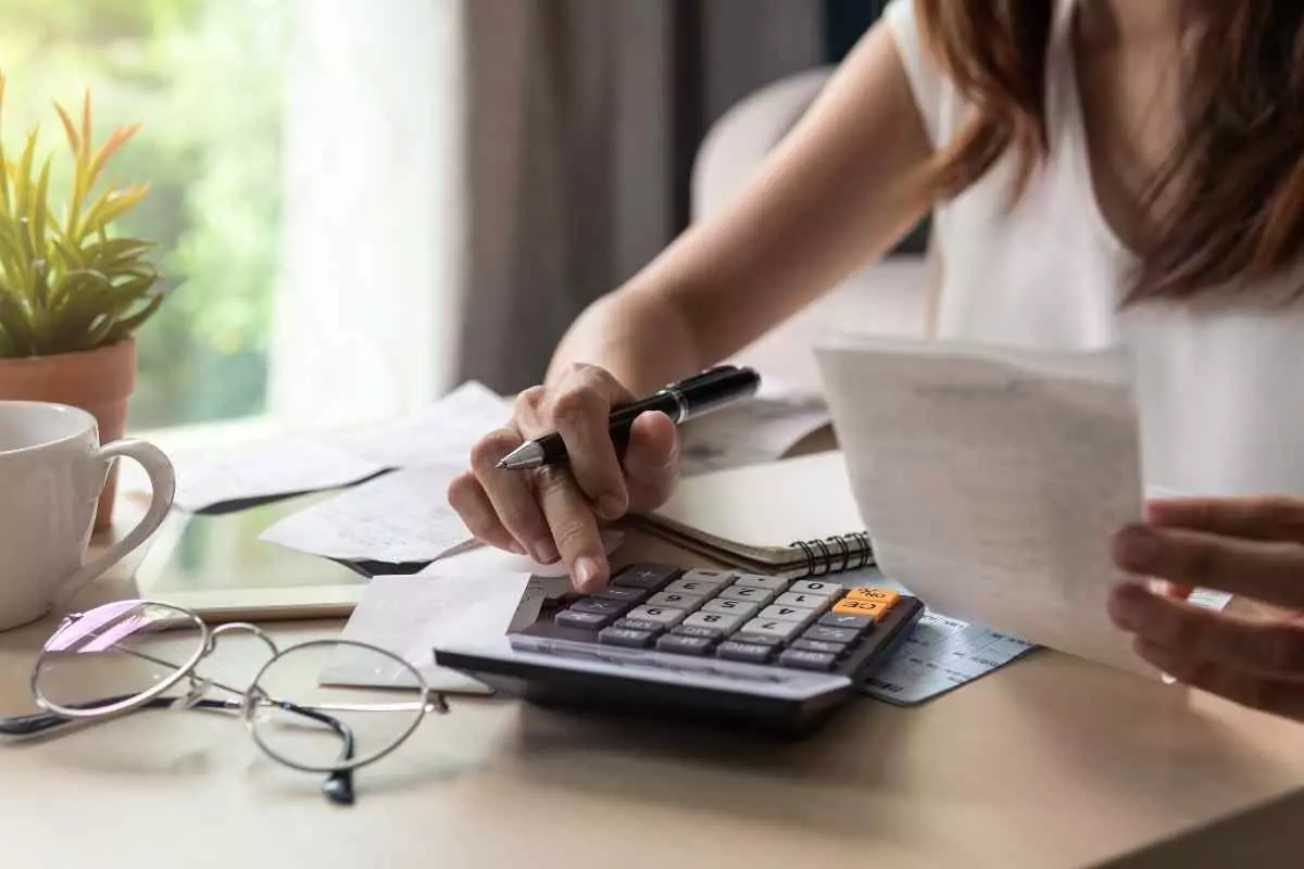 Close up of young adult holding receipt and using calculator.