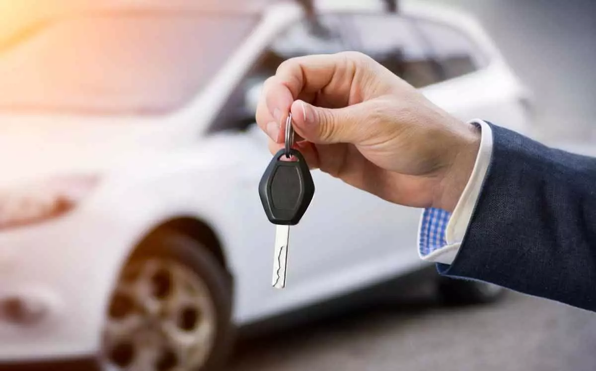 Borrower holding car key in front of new car