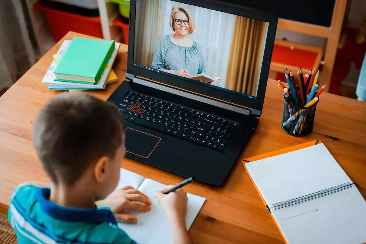 A child sitting at a desk with a laptop and a pen, focused on studying