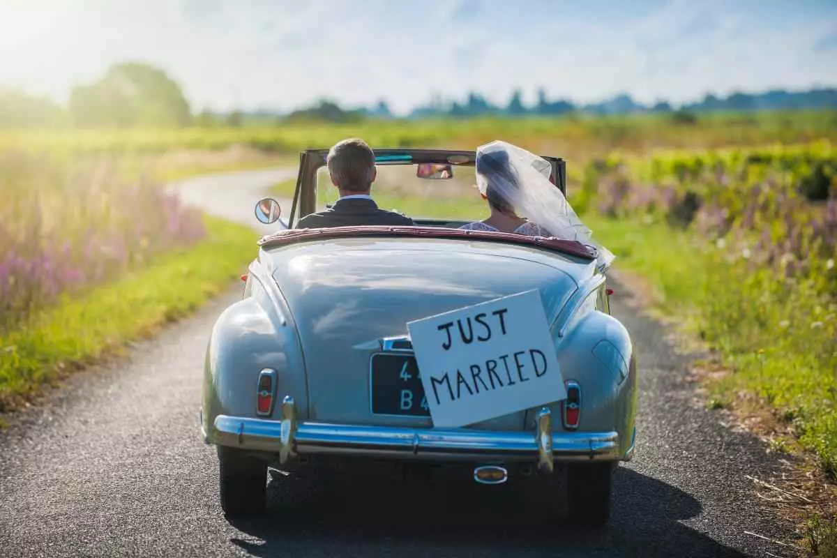 Married couple driving away in a car with a "just married" sign.