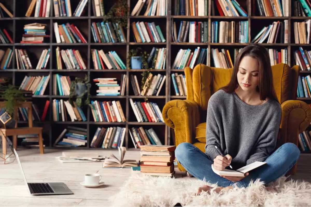 Woman sitting at desk with laptop in front of bookcase, focused on writing
