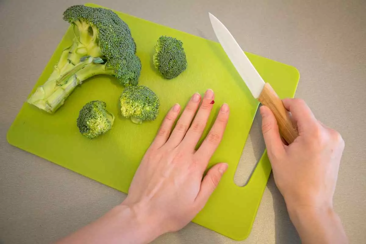 Wounded finger with blood and knife on cutting board with broccoli