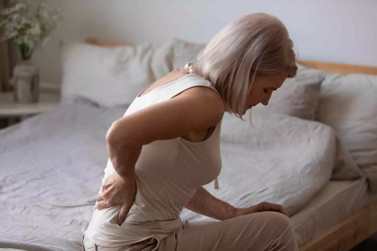 A woman sitting on a bed with her hand on her back.