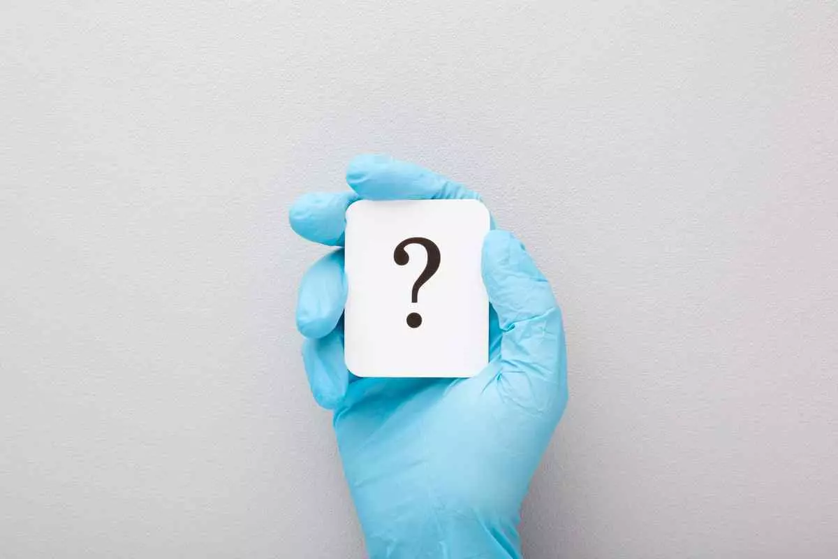 A hand in blue gloves holding a white card with a question mark on it