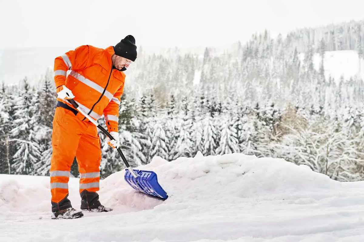 A man in an orange jacket shoveling snow