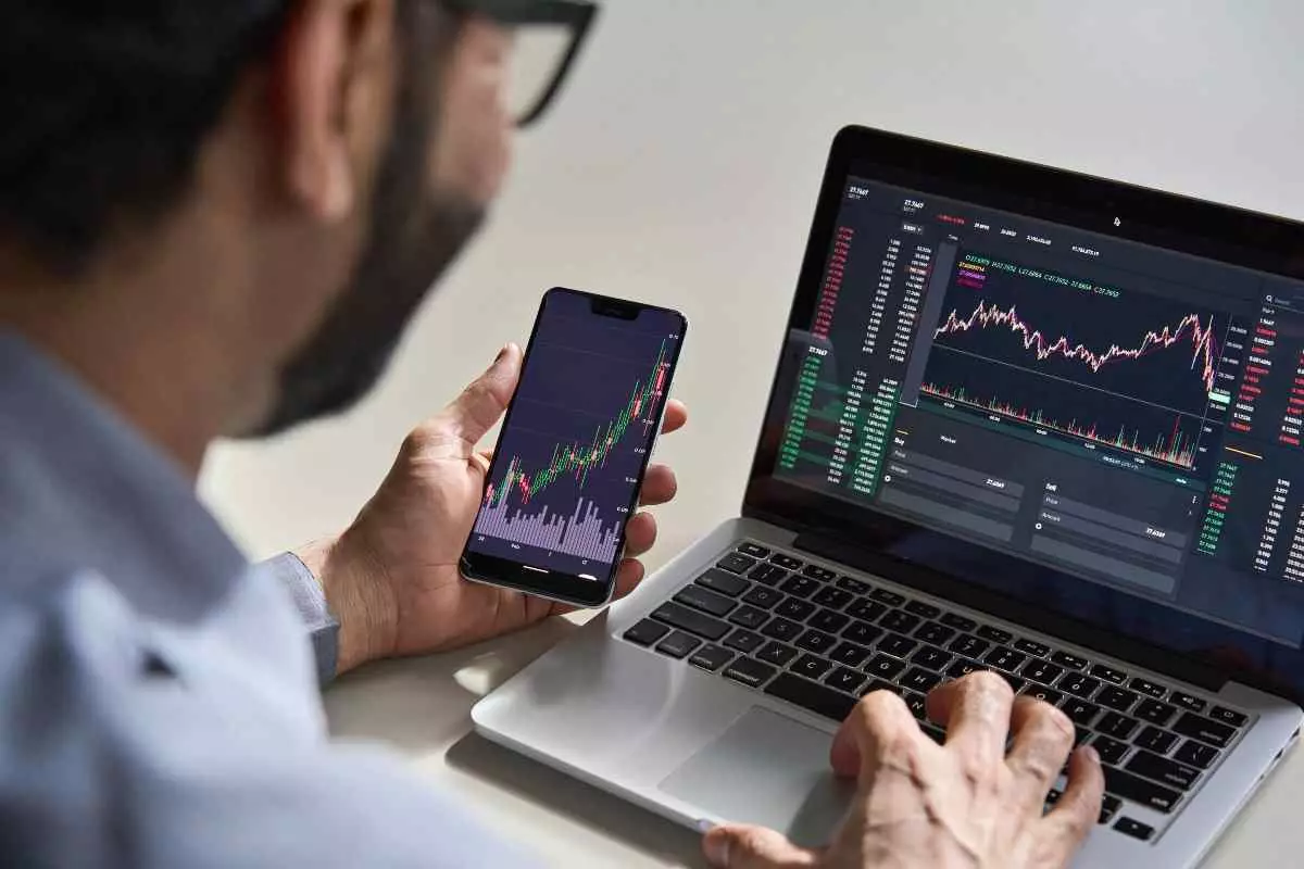 Individual investing in stocks on cellphone and laptop.