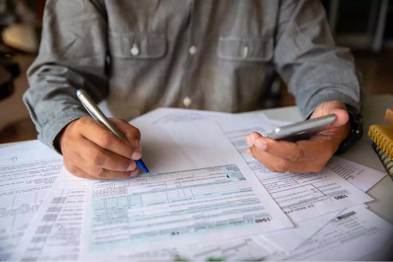 Closeup of individual holding phone and completing tax paperwork.