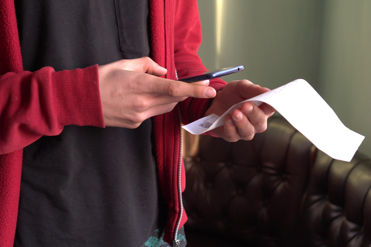 A person holding their phone up to a receipt to track their spending.