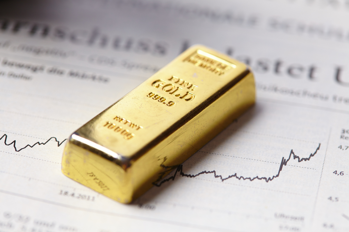 A gold bar laying on top of stocks news article. 