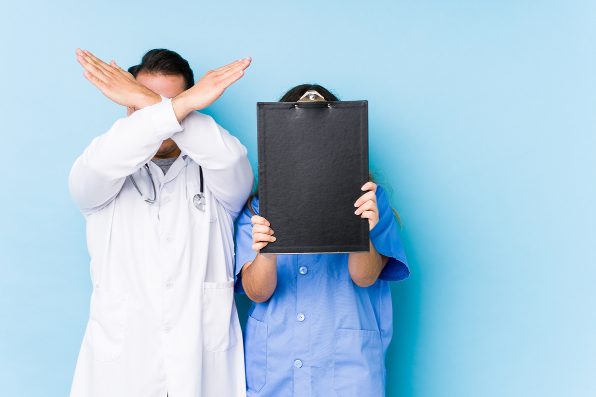A doctor and nurse protecting themselves with their hands across their face.