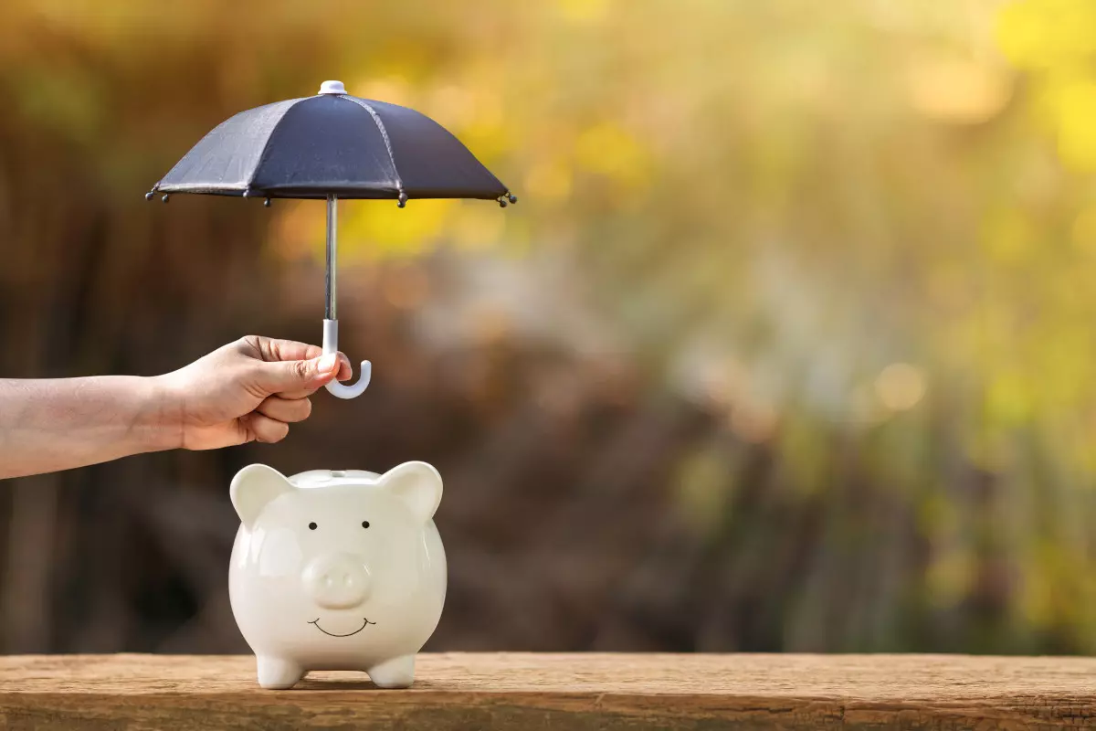 A hand holding an umbrella over a piggy bank. 