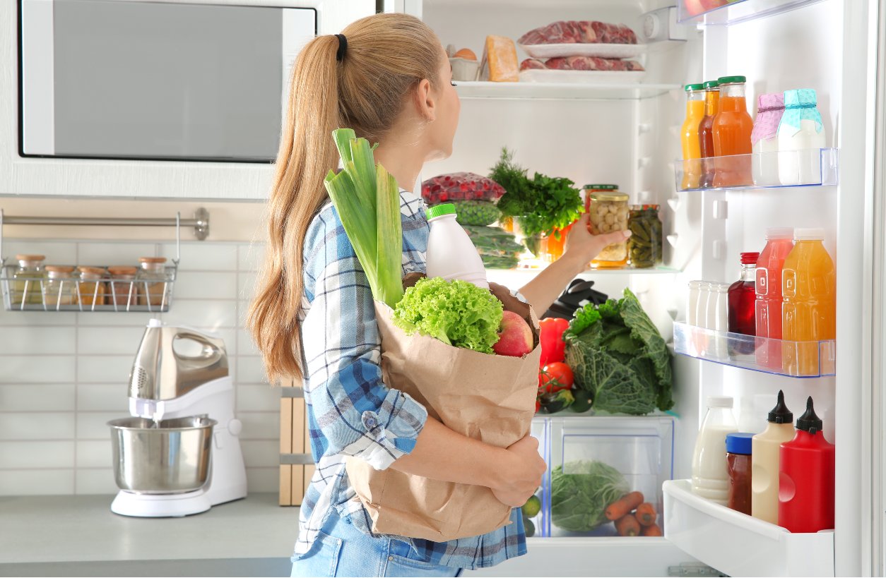 Young adult storing groceries in refrigerator.