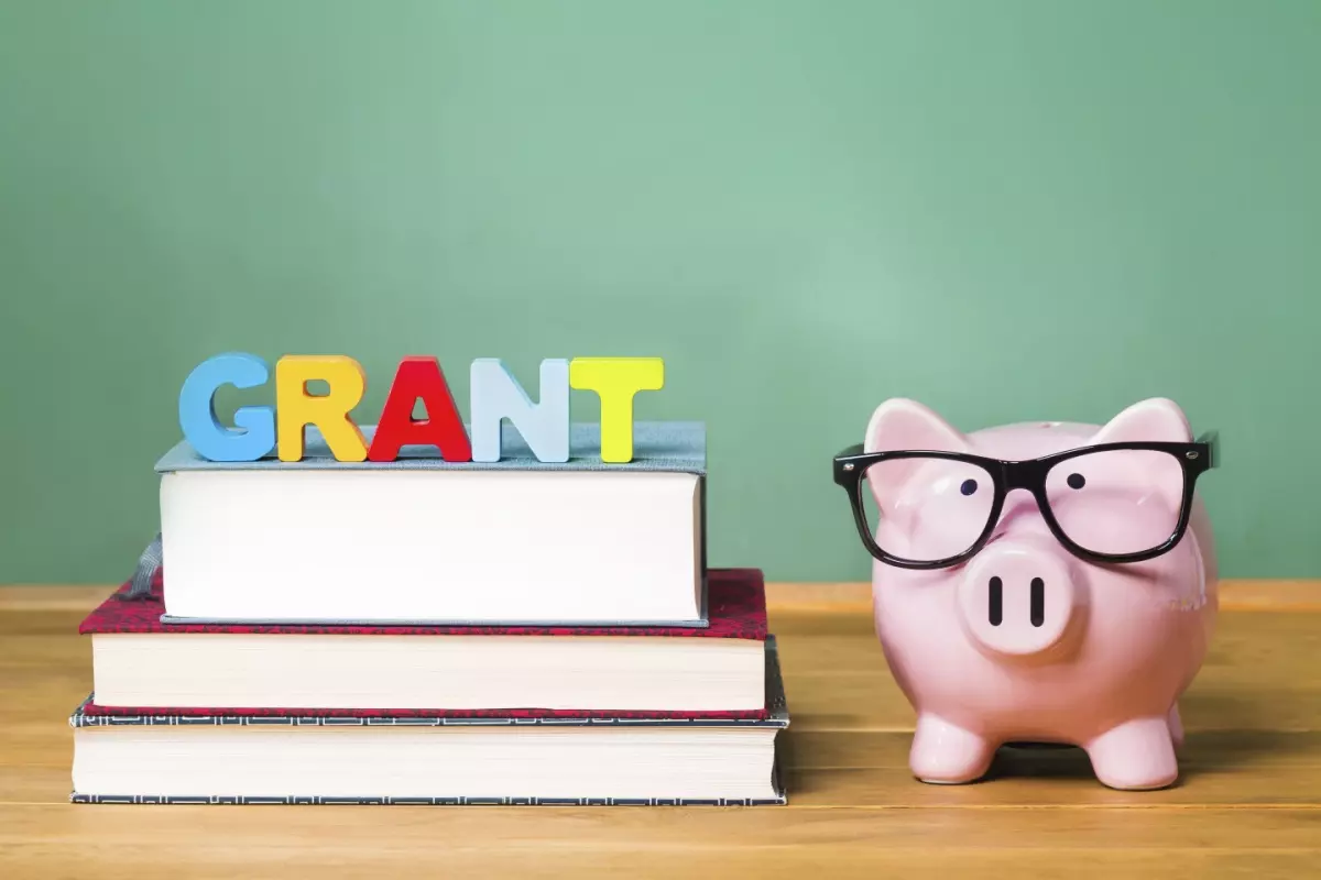 Stack of books with "grant" blocks and piggy bank with glasses